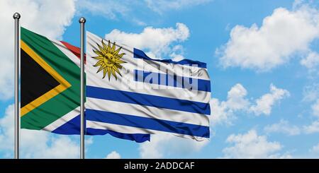 L'Afrique du Sud et l'Uruguay drapeaux dans le vent contre ciel bleu nuageux blanc ensemble. Concept de diplomatie, de relations internationales. Banque D'Images