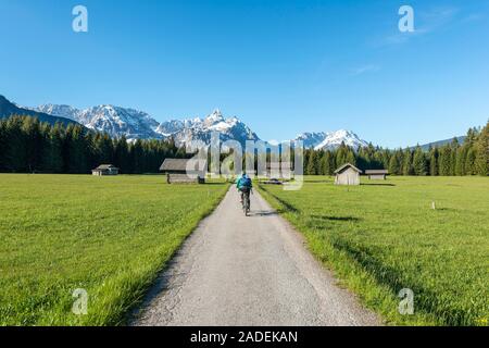 Frau radelt, granges à foin dans un pré, et les montagnes, d''Ehrwalder Sonnenspitz près de Ehrwald, Tyrol, Autriche Banque D'Images