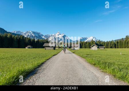 Frau radelt, granges à foin dans un pré, et les montagnes, d''Ehrwalder Sonnenspitz près de Ehrwald, Tyrol, Autriche Banque D'Images