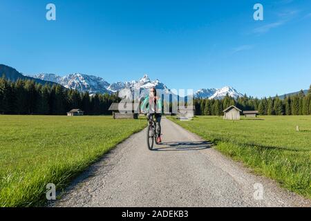 Frau radelt, granges à foin dans un pré, et les montagnes, d''Ehrwalder Sonnenspitz près de Ehrwald, Tyrol, Autriche Banque D'Images