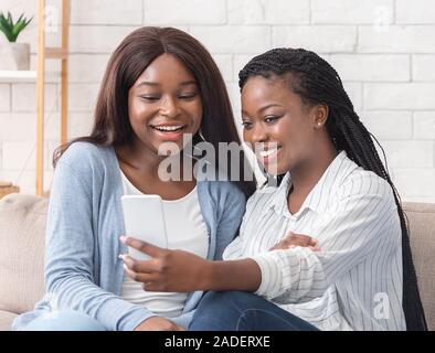 Deux copines noir joyeux en tenant de selfies at home Banque D'Images