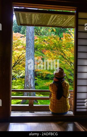 Une femme assise dans la maison traditionnelle en bois avec de belles feuilles érable coloré d'automne dans le jardin. Banque D'Images