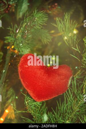 Coeur fait main lin rouge décoration pendaison sur arbre de Noël sur l'arrière-plan de feux lumineux guirlande de noël, cadre vertical Banque D'Images