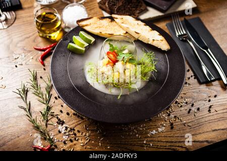 Ceviche de pétoncle à la mangue, au piment et à la coriandre servie dans une assiette avec de la fumée de glace liquide. Délicieux aliments sains servis pour le déjeuner sur une table Banque D'Images