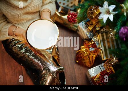 Gros plan sur 40 ans, femme, et dans l'or paillette jupe et pull blanc sous l'arbre de Noël décoré des boîtes près de l'actuel vide holding plaque. Banque D'Images