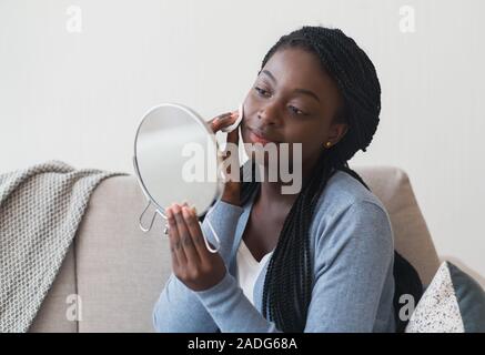 Fille noire à la recherche de miroir et visage nettoyage avec un coton Banque D'Images