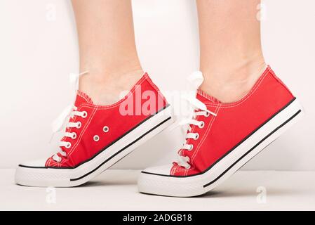 Pieds de femme en rouge gumshoes sur fond blanc. Banque D'Images