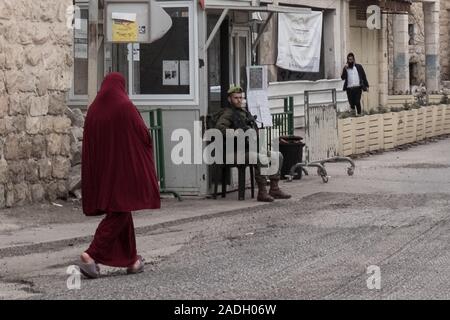 Hébron, en Cisjordanie. 4 Décembre, 2019. Un soldat surveille la rue à Hébron, séparant symboliquement une femme palestinienne et un homme Juif. Le Ministre israélien de la Défense, Bennett a récemment annoncé son approbation de la création d'un nouveau quartier juif dans la ville palestinienne d'Hébron principalement près de l'ancien marché de fruits et légumes. La terre, achetés par des Juifs vivant là au début du 19e siècle, a été abandonné après le massacre de 1929 où 67 Juifs ont été assassinés par les émeutiers arabes. Credit : Alon Nir/Alamy Live News. Banque D'Images