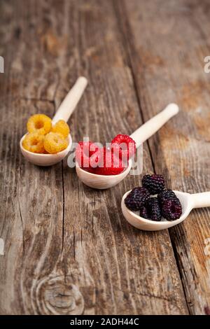 Fruits rouges et jaunes, les framboises et les mûres dans les cuillères sur une vieille table en bois. De délicieux petits fruits. Banque D'Images