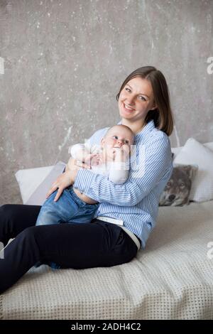 Happy Young Caucasian Family en studio. La mère est tenue et serrant sa petite fille dans les mains. Beau Les gens assis sur le lit. Femme souriante. Infan Banque D'Images