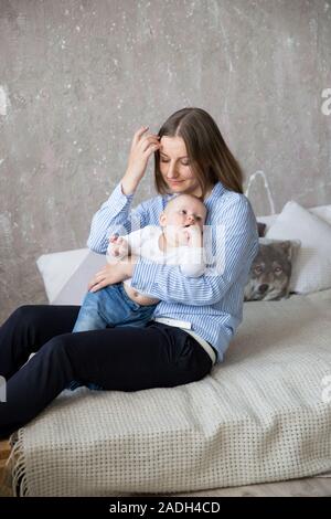 Happy Young Caucasian Family en studio. La mère est tenue et serrant sa petite fille dans les mains. Beau Les gens assis sur le lit. Femme souriante. Infan Banque D'Images