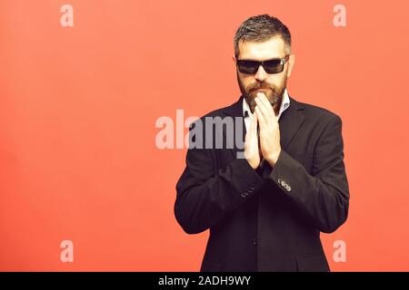 Succès d'affaires et de concept. Homme à barbe sombre et en costume classique. Businessman détient les mains ensemble, l'espace de copie. Guy avec visage concentré et lunettes isolé sur fond rose saumon Banque D'Images