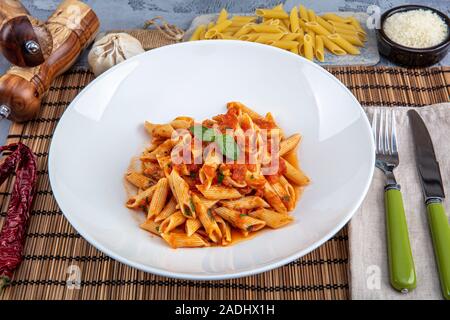 Pâtes penne avec sauce chili sauce arrabiata. L'arrabiata penne italienne classique avec le basilic et le fromage pecorino fraîchement râpé sur une table en bois rustique. Banque D'Images