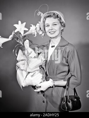 1950 ÉLÉGANT SMILING WOMAN LOOKING AT CAMERA WEARING HAT TAILLEUR GANTS BLANCS HOLDING POCKET BOOK et Lis de Pâques - e415 HAR001 HARS JOIE DE VIE RELIGION CÉLÉBRATION DE PÂQUES FEMELLES DEMI-LONGUEUR DE LUXE MESDAMES LES PERSONNES QUI S'OCCUPENT DE LA SPIRITUALITÉ DES EXPRESSIONS DE CONFIANCE B&W CONTACT DES YEUX LE BONHEUR ET LA FIERTÉ DES STYLES JOYEUX SOURIRES JOYEUX CONCEPTUEL LILY LYS SUR MESURE ÉLÉGANT MI-MODE MI-ADULTES FEMME ADULTE NOIR ET BLANC DE L'ORIGINE ETHNIQUE CAUCASIENNE HAR001 LIVRE DE POCHE à l'ANCIENNE Banque D'Images