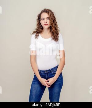 Belle jeune fille sérieuse en pleine croissance sur fond beige regarde droit, les cheveux bouclés brun Banque D'Images