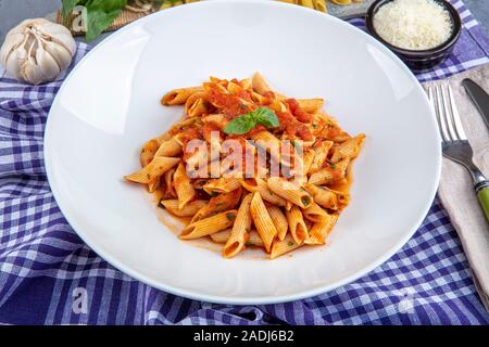 Pâtes penne avec sauce chili sauce arrabiata. L'arrabiata penne italienne classique avec le basilic et le fromage pecorino fraîchement râpé sur une table en bois rustique. Banque D'Images