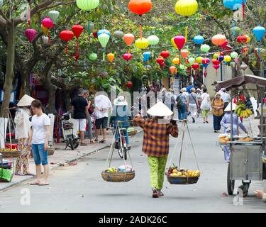 Vendeur de fruits avec chapeau typique dans une rue de Hoi An, Vietnam Banque D'Images