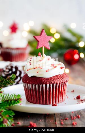 Christmas red velvet cupcakes décorée avec une star shaped cake pick, avec ornements de Noël, le sapin et l'éclairage sur une table en bois rustique Banque D'Images