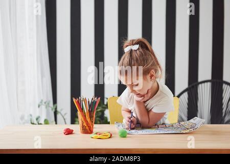 Mur avec des bandes noires derrière. Jolie petite fille dans l'école d'art attire ses premiers tableaux de crayons et marqueurs Banque D'Images