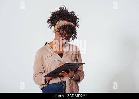 Élève écrit sur le bloc-notes. African American girl magnifique avec des cheveux bouclés dans le studio avec fond blanc Banque D'Images