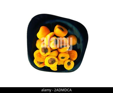 Moitiés d'abricots avec de la pierre noire sur une assiette. Le contraste des couleurs. Isoler sur fond blanc Banque D'Images