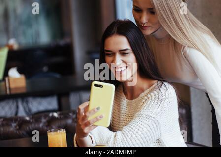 Nous allons donc vérifier notre photo. Dans le restaurant. Deux amies, m'asseoir à l'intérieur avec verre jaune et utiliser le smartphone Banque D'Images