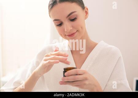 Dame calme et souriant en tenant le petit pot de crème Banque D'Images