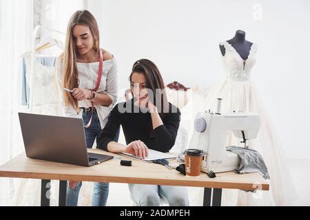 À la recherche sur l'ordinateur portable. Deux créateurs de mode féminine travaille sur les nouveaux vêtements à l'atelier Banque D'Images