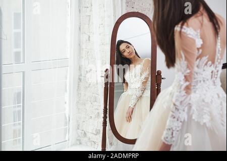 Jeune épouse regarde dans le miroir. Le processus de mise en place de la robe dans le studio de vêtements faits à la main Banque D'Images