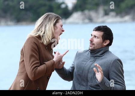 Femme en colère en criant à son mari de peur sur la plage Banque D'Images