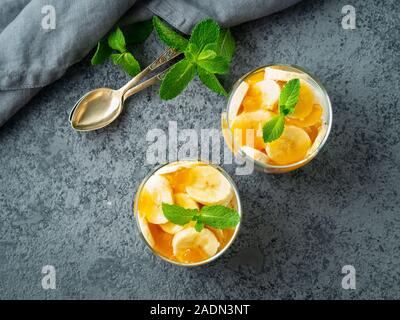 En couches avec du yaourt dessert sain, banane, mangue, cookie en verre sur fond noir en gris, vue du dessus. Banque D'Images