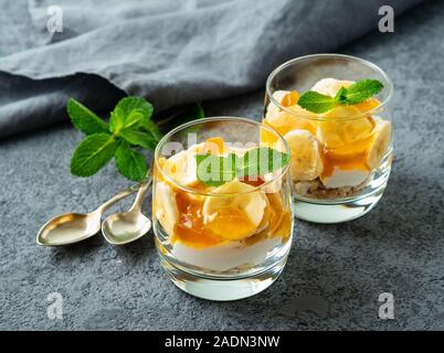 En couches avec du yaourt dessert sain, banane, mangue, cookie en verre sur fond noir en gris, vue de côté. Banque D'Images