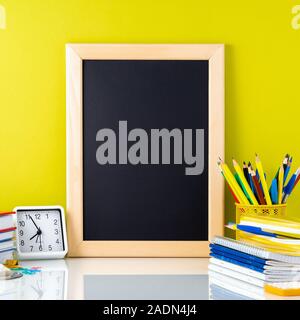 Tableau, manuels, fournitures scolaires et de l'horloge sur tableau blanc par le mur jaune. Vue de côté, l'espace vide pour le texte. Concept Retour à l'école. Banque D'Images