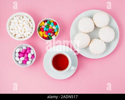 Tasse de thé, des plaques de différents bonbons - guimauves, sucettes, bonbons. Les glucides, le glucose. Fond rose Banque D'Images