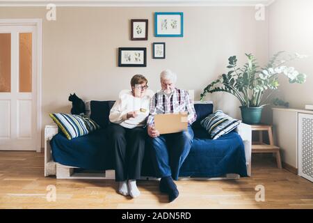 Personnes âgées Caucasian couple faisant achats en ligne sur le canapé à la maison, regardant un écran d'ordinateur portable et souriant Banque D'Images