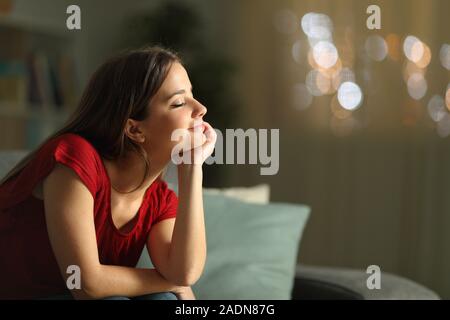 Vue latérale d'un portrait relaxed woman meditating seul assis sur un canapé à la maison dans la nuit Banque D'Images