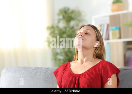 Satisfait woman meditating respirer l'air frais à l'aide d'écouteurs sans fil, assis sur un canapé dans la salle de séjour à la maison Banque D'Images