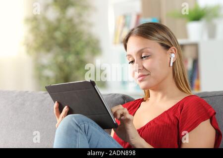 Femme à l'aide d'e-learning tablet et écouteurs sans fil assis sur un canapé dans la salle de séjour à la maison Banque D'Images