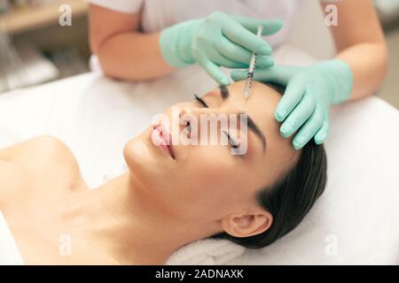 Les mains dans les gants holding syringe avec lors de l'injection d'acide hyaluronique Banque D'Images