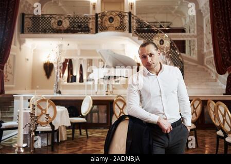Portrait de guy dans l'usure officielle se tient dans le magnifique restaurant en style vintage avec piano sur la scène Banque D'Images
