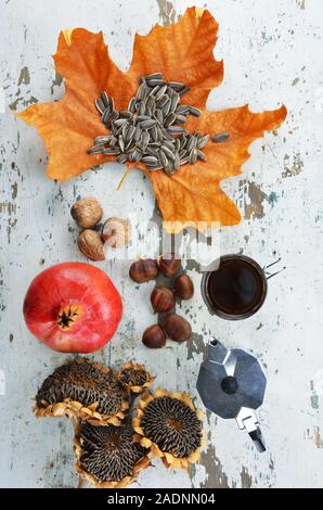 Tasse de café noir, café,une feuille de platane avec quelques graines de tournesol , une grenade,tournesols séchés,les châtaignes et les noix sur une vieille table en bois Banque D'Images