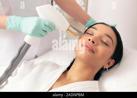 Femme pacifique fermant les yeux pendant le traitement laser moderne Banque D'Images