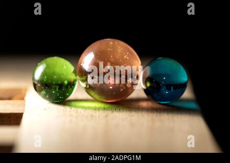 Un portrait de trois marbres de différentes couleurs sur une surface en bois coloré casting réflexions. Les sphères de verre sont l'orange, vert et bleu. Banque D'Images