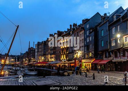 Bateaux à quai dans le vieux port de Honfleur, France avec ses terrasses de café à l'heure bleue Banque D'Images