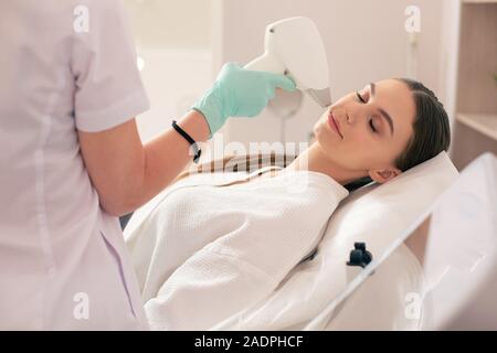 Femme en fermant les yeux et avoir l'enlèvement de cheveux de laser sur son visage Banque D'Images