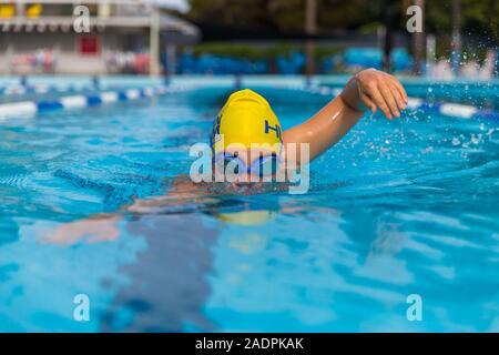 Une femme nageant dans une piscine publique avec un chapeau et des lunettes de natation jaune faisant le crawl freestyle nager avc. Banque D'Images