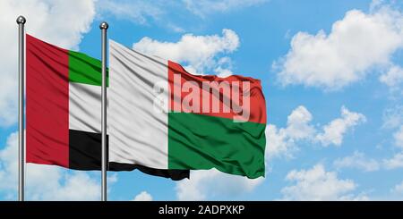 Emirats Arabes Unis et de brandir le drapeau de Madagascar dans le vent contre ciel bleu nuageux blanc ensemble. Concept de diplomatie, de relations internationales. Banque D'Images