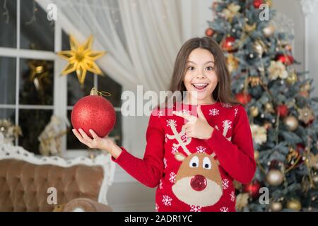 Le rouge est mon préféré. Décor d'attributs de Noël. Petite fille près de l'arbre de Noël. Enfant célébrer Noël à la maison. Traditions d'hiver. Adorable gamin excité porter le chandail de noël. Boutique cadeaux concept. Banque D'Images