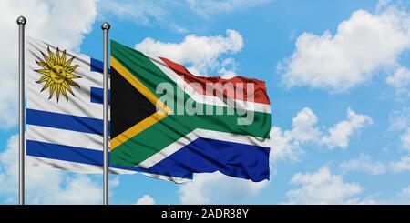L'Uruguay et l'Afrique du Sud drapeaux dans le vent contre ciel bleu nuageux blanc ensemble. Concept de diplomatie, de relations internationales. Banque D'Images