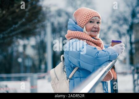 Senior woman in blue winter coat holding tasse de café en plein air Banque D'Images
